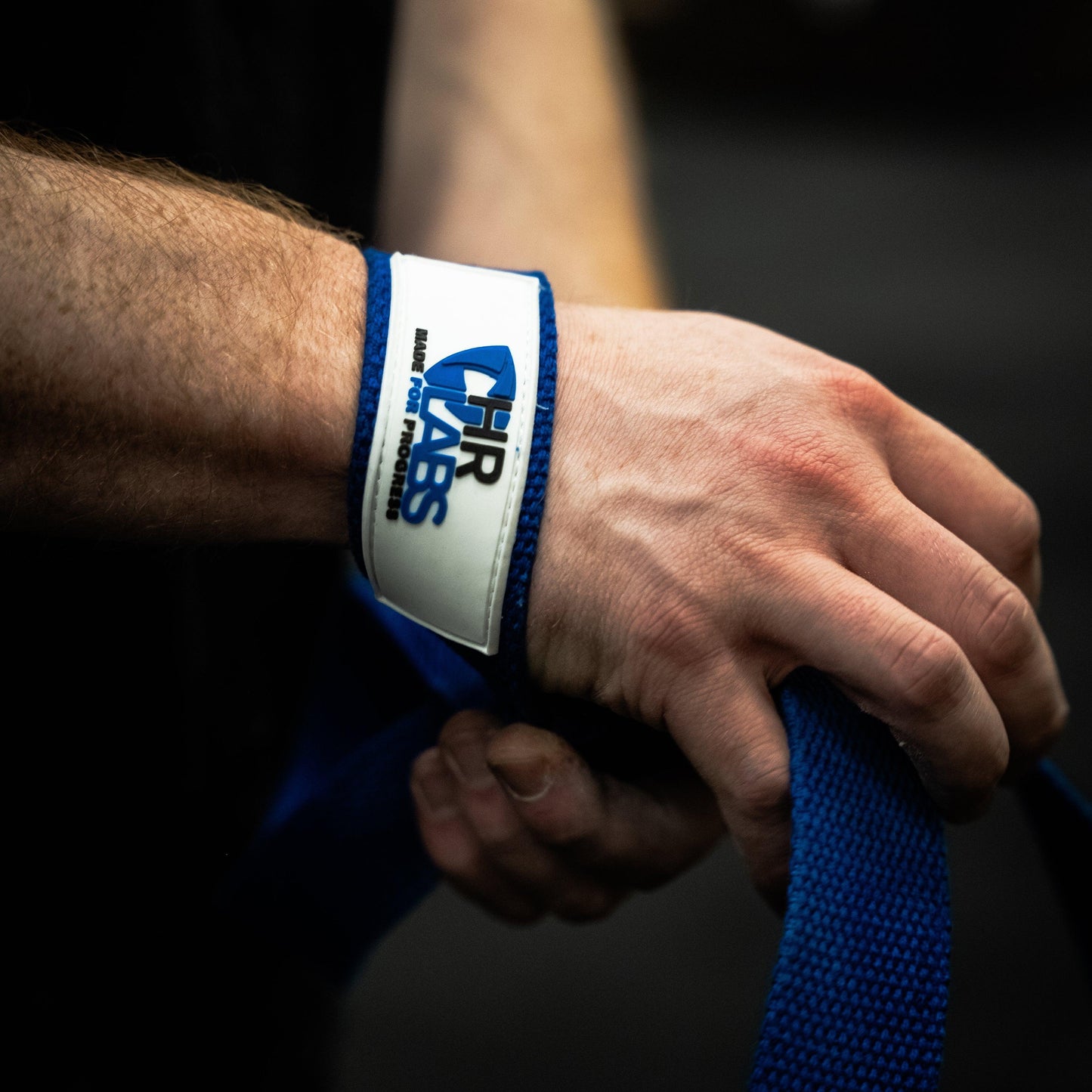 Hand gripping blue gym lifting strap with visible wrist support, close-up